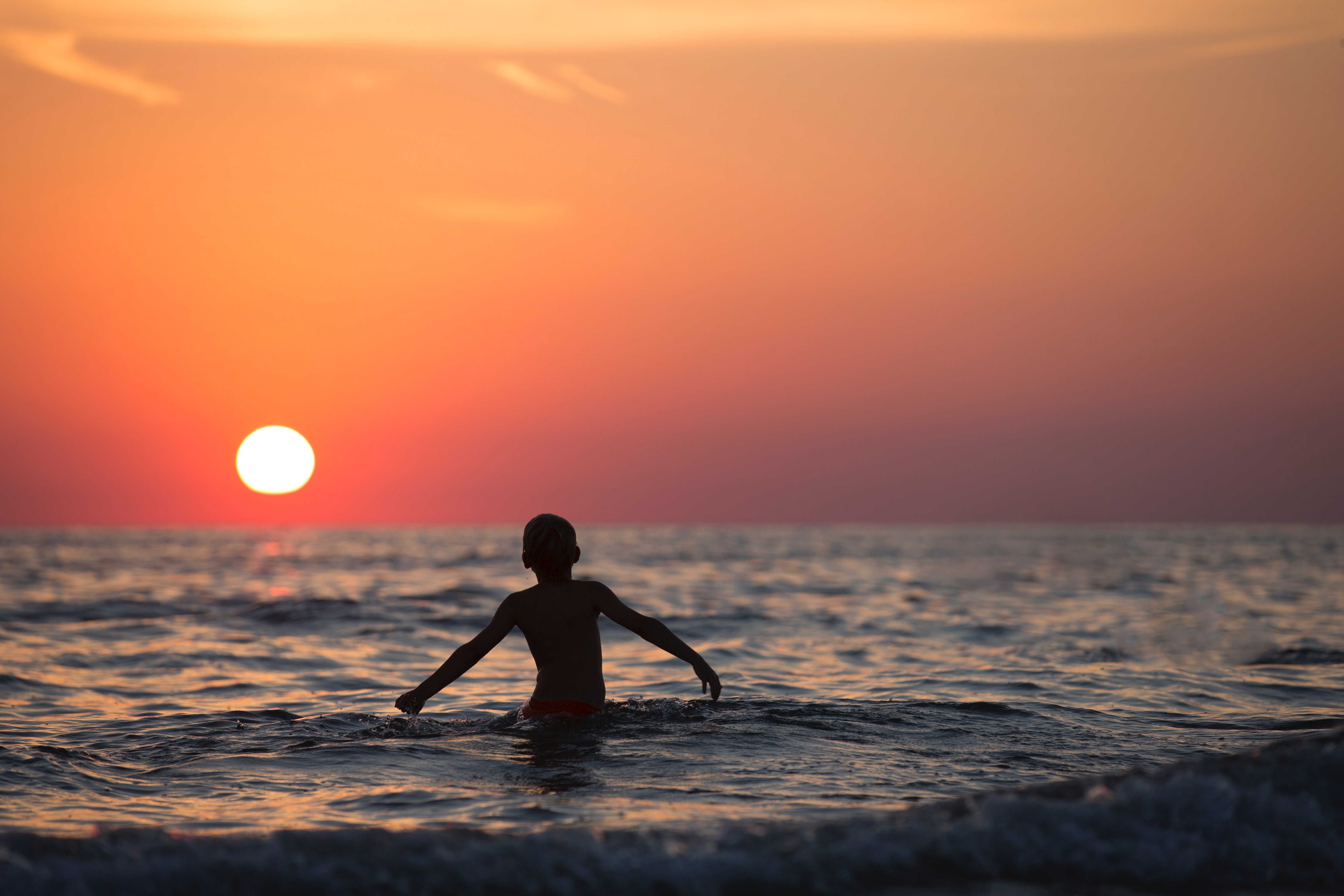 Silhouette photo of child on body of water during golden hour